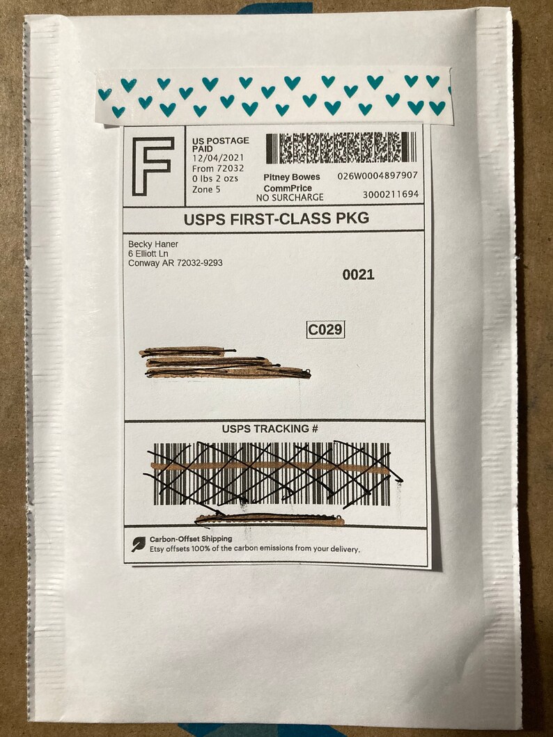 May include: White envelope with a USPS First-Class Package label. The label includes the sender's name, address, and the recipient's name and address. The label also includes the tracking number, postage paid information, and the date of mailing. The envelope has a green leaf icon with the text "Carbon-Offset Shipping" and "Etsy offsets 100% of the carbon emissions from your delivery."