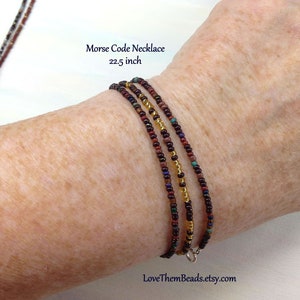 May include: A multi-strand necklace made of small, colorful beads in shades of brown, gold, and red. The necklace is 22.5 inches long and has a silver clasp.  Morse Code Necklace 22.5 inch LoveThemBeads.etsy.com