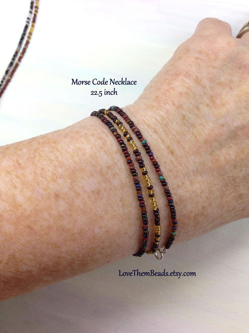 May include: A multi-strand necklace made of small, colorful beads in shades of brown, gold, and red. The necklace is 22.5 inches long and has a silver clasp.  Morse Code Necklace 22.5 inch LoveThemBeads.etsy.com