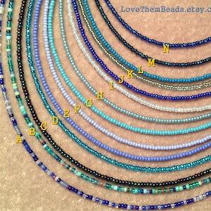 May include: A variety of 14 different shades of blue and turquoise seed bead necklaces, labeled A through N. The necklaces are arranged in a semi-circle, with the smallest necklace at the top and the largest necklace at the bottom.