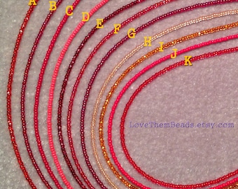 May include: A set of 12 strands of seed beads in various shades of red, pink, and orange. The beads are arranged in a semi-circle, with the largest strand at the top and the smallest strand at the bottom. The strands are labeled with letters from A to K.