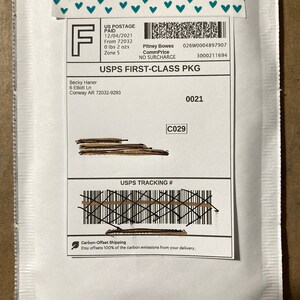 May include: White envelope with a USPS First-Class Package label. The label includes the sender's name, address, and tracking number. The label also includes the text "USPS First-Class Package" and "NO SURCHARGE".