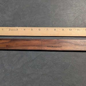 May include: A wooden ruler with markings from 1 to 13 inches. The ruler is made in the USA. Below the ruler is a dark brown wooden piece with the text "Scotts Mountain Crafts" engraved on it.