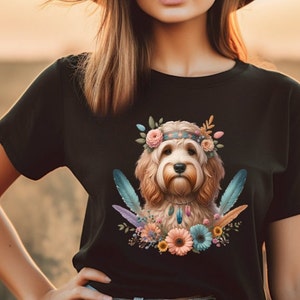 May include: A black t-shirt with a colorful illustration of a dog wearing a flower crown and feathers. The dog is a light brown color with a white chest and a black nose.