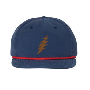 Könnte beinhalten: Marineblaue Baseballkappe mit einem braunen Blitz-Design auf der Vorderseite. Die Kappe hat eine rote Kordel am Rand. Ein lässiges Accessoire.