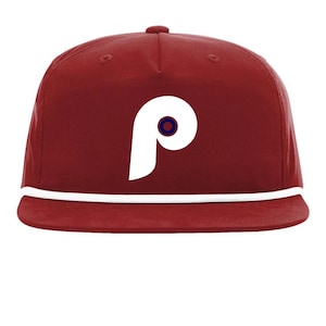 Könnte beinhalten: Burgunderfarbene Baseballkappe mit weißem "P"-Logo und einem marineblauen Kreis. Die Kappe hat ein weißes Seildetail am Rand. Ein stilvolles Accessoire für Sportfans.