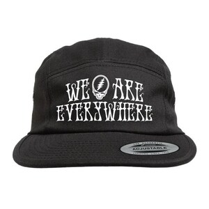 May include: A black five-panel cap featuring the white text WE ARE EVERYWHERE with a lightning bolt skull icon in the centre. The hat has a flat brim and a silver-toned sticker on the brim that reads THE AUTHENTIC ADJUSTABLE YUPOONG SINCE 1974.
