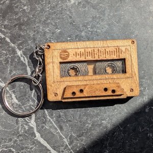 May include: Wooden cassette tape keychain with a silver keyring. The keychain features a laser-etched design of a sound wave and the Spotify logo. The cassette tape design includes visible tape reels and a detailed appearance.