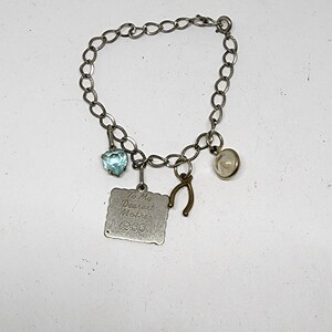 May include: A silver charm bracelet with a variety of charms, including a heart-shaped charm with a blue stone, a horseshoe charm, a small round charm with a clear stone, and a square charm with the inscription "To My Dearest Mother 1966".