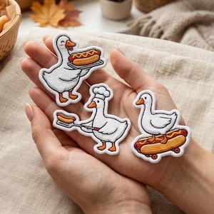 May include: Three embroidered patches featuring white geese with orange beaks and feet. One goose holds a hot dog on a tray, another wears a chef hat and holds a hot dog on a spatula, and the third goose stands on a hot dog shaped like a skateboard.