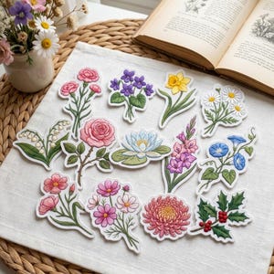 May include: A collection of thirteen embroidered flower patches featuring various botanical designs including a pink rose, yellow daffodil, blue lotus, white daisies, purple violets, lily of the valley, pink carnations, and holly with red berries.