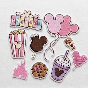 May include: A collection of embroidered patches featuring a pink and white striped popcorn bucket, a brown chocolate-covered ice cream bar, pink Mickey-shaped balloons, a churro, a pink castle, a chocolate chip cookie, a drink, and a pink cotton candy.