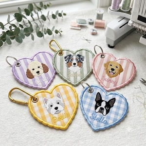 May include: Five heart-shaped fabric keychains with embroidered dog portraits and names. The keychains feature pastel gingham patterns in purple, green, pink, yellow, and blue, each with a metal lobster clasp and stitched scalloped edges.