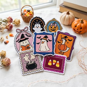 May include: A collection of seven embroidered patches featuring Halloween themes, including ghosts, a pumpkin, a duck in a pumpkin costume, a cauldron, and candy corn. The patches are shaped like ornate frames, stamps, and ovals with colorful thread.