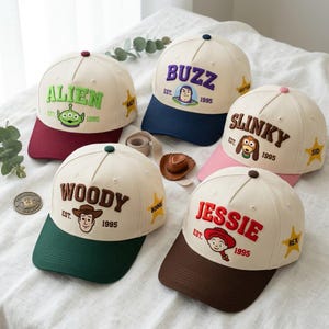 Peut inclure: Cinq casquettes de baseball représentant des personnages de Toy Story. Chaque casquette crème a une visière colorée, le nom du personnage brodé, son visage, le texte EST. 1995 et une étoile avec un nom comme Andy, Sid, Bonnie ou Rex.