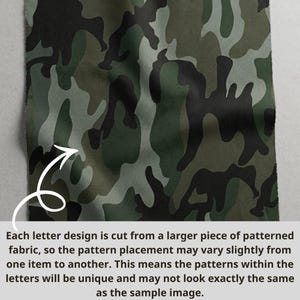 May include: A piece of camouflage fabric in shades of green, brown, and black. The fabric has a repeating pattern of irregular shapes. Text on the image explains that the pattern placement may vary slightly from one item to another.