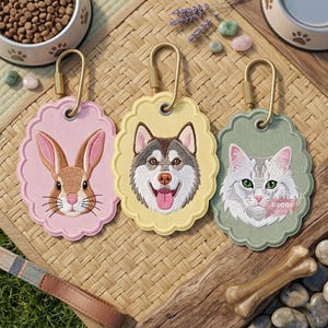 May include: Three oval-shaped embroidered pet tags with scalloped edges and gold-tone carabiner clips. The pink tag features a brown rabbit, the yellow tag shows a husky dog, and the sage green tag displays a grey and white cat with green eyes.
