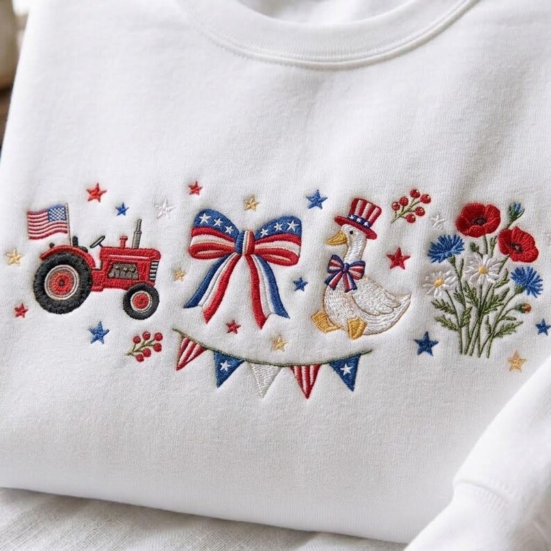 K&ouml;nnte beinhalten: Wei&szlig;es Sweatshirt mit gestickten patriotischen Designs. Mit einem roten Traktor mit amerikanischer Flagge, einer Schleife, einer Gans mit Zylinder, Blumen und Stern- und Bannerakzenten. Ein festliches Kleidungsst&uuml;ck im Americana-Stil.