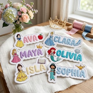 May include: Six embroidered fabric name patches featuring cartoon characters and icons. The patches display the names AVA with an apple, CLARA with a glass slipper, MAYA with a crown, OLIVIA with a seashell, ISLA with a book, and SOPHIA with a lamp.