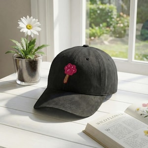 May include: A white ceramic mug with a black handle and the text "But First, Coffee" in a bold, black font. The mug is set against a blurred background, suggesting a cozy setting.