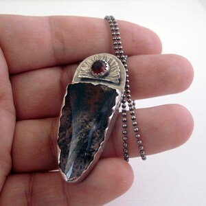 May include: A silver pendant necklace with a dark gray and white agate stone, a red gemstone, and a silver chain.