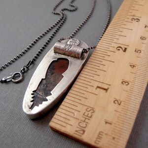 May include: A silver pendant with a red and brown stone set in a cutout design. The pendant is 1 3/4 inches long and is on a silver chain. The pendant is marked "AM Gilbert 925".