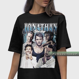 May include: Black t-shirt with a vintage-style graphic featuring a group of four men and the text "JONATHAN Bailey".