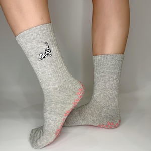 May include: A pair of grey gripper socks with pink dots on the bottom. One sock has a black and white cat design on the side.