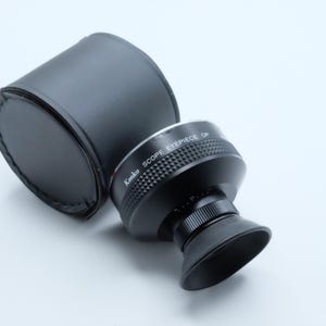 May include: A black Kenko scope eyepiece with a rubber eye cup and a matching black leather case. The eyepiece has the text "Kenko SCOPE EYEPIECE OP" printed on it. The eyepiece is designed for use with a telescope or spotting scope.