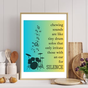 Può includere: Una stampa incorniciata con uno sfondo sfumato giallo e blu. La stampa presenta una silhouette nera di una batteria con note musicali. Il testo "chewing sounds are like tiny drum solos that only irritate those with an ear for SILENCE" è stampato in nero sul lato destro della stampa.