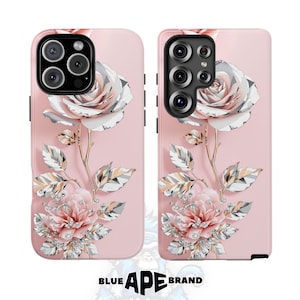 Puede incluir: Dos fundas rosas para teléfono con un diseño floral. Cada funda presenta una gran rosa blanca y rosa con tallos y hojas doradas. El diseño incluye un grupo de flores rosas y acentos brillantes. La marca "BLUE APE BRAND" está en la parte inferior.