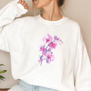 Peut inclure: Sweat-shirt blanc avec un imprimé d'orchidée aquarelle rose et violet.