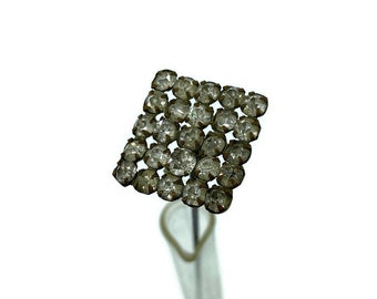 May include: A vintage rhinestone pin with a square shape and a silver tone finish. The pin is adorned with clear rhinestones.