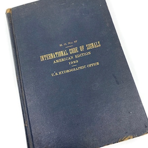 May include: A navy blue hardcover book titled "International Code of Signals, American Edition, 1923, U.S. Hydrographic Office".