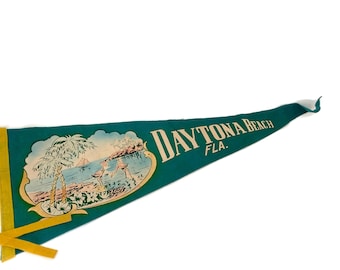 May include: A vintage pennant in teal green with the words "DAYTONA BEACH FLA." in gold lettering. The pennant features a scenic illustration of a beach with palm trees and figures. Yellow ribbon is attached.