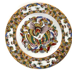 May include: A white ceramic plate featuring a colourful butterfly design. The plate has a yellow border with a repeating pattern of butterflies. The centre of the plate showcases a large butterfly with intricate details in shades of red, blue, green, and yellow.