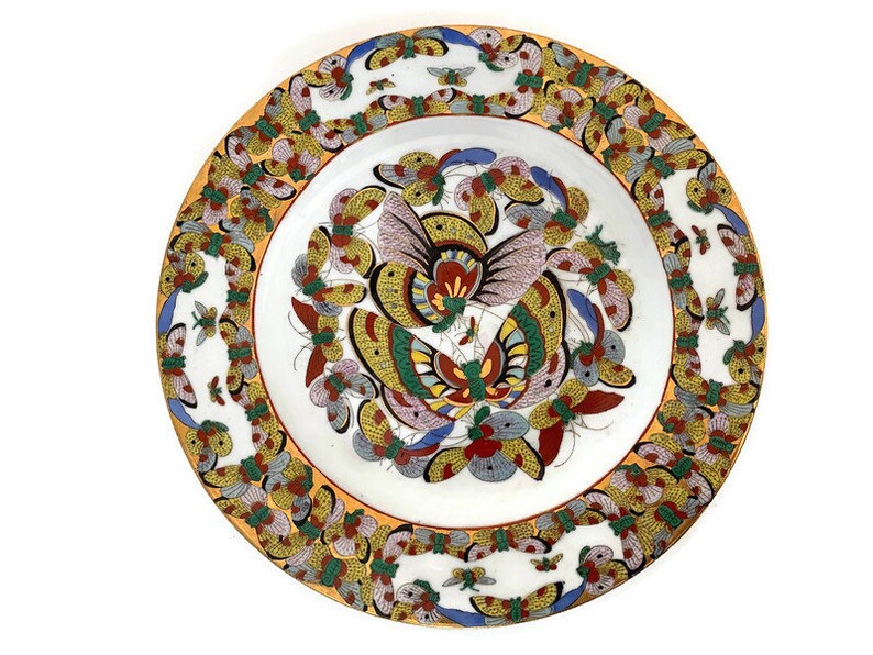 May include: A white ceramic plate featuring a colourful butterfly design. The plate has a yellow border with a repeating pattern of butterflies. The centre of the plate showcases a large butterfly with intricate details in shades of red, blue, green, and yellow.
