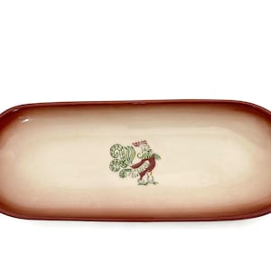 May include: An oval-shaped serving platter with a rooster design. The platter has a cream-colored center and a reddish-brown rim. The rooster is depicted in red, green, and white. This decorative platter is suitable for serving food.