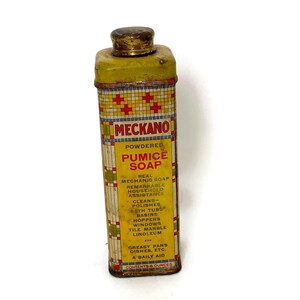 May include: A yellow metal tin with a red and blue checkered pattern. The tin contains powdered pumice soap. The label reads "MECKANO Powdered Pumice Soap Real Mechanic Soap Remarkable Household Assistance Cleans-Polishes Bath Tubs Basins Hoppers Windows Tile Marble Linoleum Greasy Pans Dishes, Etc. A Daily Aid Contents 6 Ounces"