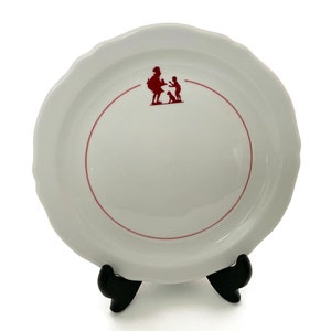 May include: White ceramic plate with a red rim and a red silhouette of a woman and child with a dog in the center.