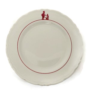 May include: White ceramic plate with a scalloped edge and a red rim. A red silhouette of a person and child is at the top. The plate is round and has a simple, elegant design.