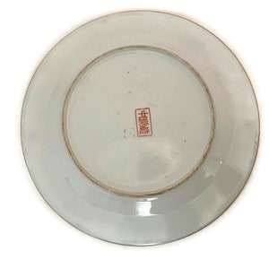 May include: White porcelain plate with a red Chinese character mark on the bottom. The plate has a raised rim and a smooth surface.