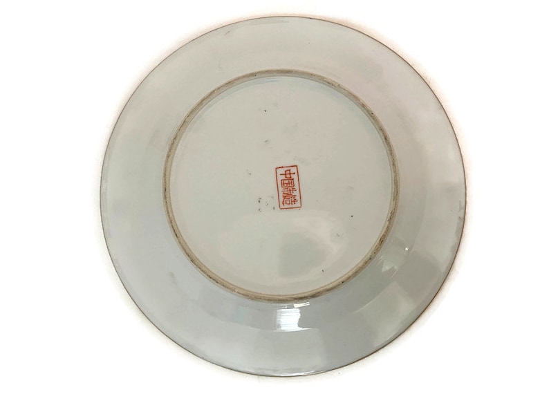 May include: White porcelain plate with a red Chinese character mark on the bottom. The plate has a raised rim and a smooth surface.