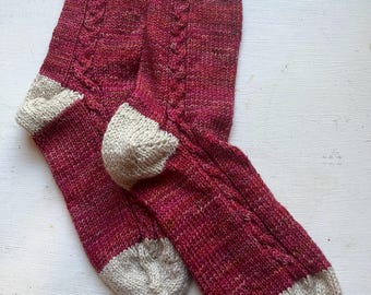 May include: A pair of knitted socks in a deep red colour with a white cable pattern. The socks have a white cuff and toe.