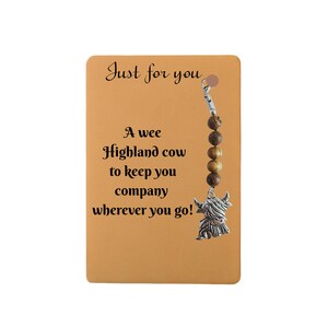 May include: A rectangular card with the text "Just for you" and "A wee Highland cow to keep you company wherever you go!" A charm with a Highland cow pendant and wooden beads hangs from the card.