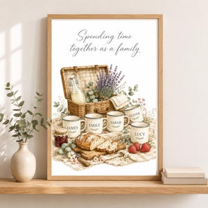 May include: A framed wall art print featuring the text 'Spending time together as a family' above a picnic scene with a wicker basket, lavender, a glass bottle, a loaf of bread, strawberries, and five white mugs personalized with the names James, Emily, Sarah, Oliver, and Lucy.