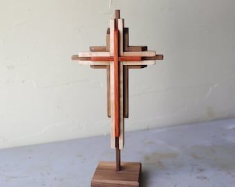 May include: A wooden cross made of multiple pieces of wood, with a red center and a natural wood finish. The cross is mounted on a wooden base.