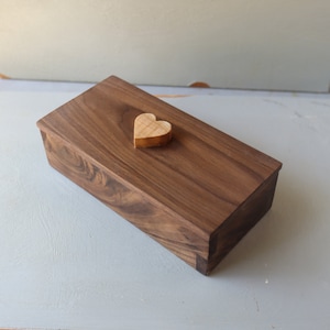 May include: A wooden box with a heart-shaped wooden lid. The box is made of dark wood with a natural finish.