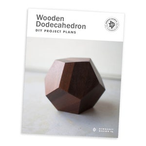 May include: DIY plans for a wooden dodecahedron, a geometric shape with 12 faces. The dodecahedron is made of dark wood and is sitting on a white surface.