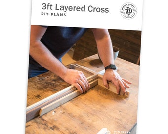 May include: A person assembling a 3ft layered cross DIY project. The cross is made of wood and is being assembled on a wooden table. The image includes the text "3ft Layered Cross DIY PLANS".